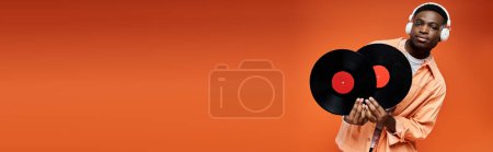 Téléchargez les photos : A fashionable young African American man holding a record against an orange backdrop. - en image libre de droit