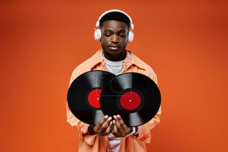 Handsome African American man in stylish attire holding a record and listening with headphones.