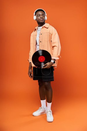 Modischer afroamerikanischer Mann mit einer Schallplatte auf orangefarbenem Hintergrund.