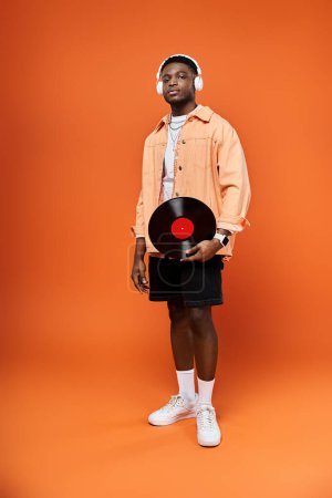 Fashionable African American man holds record on bright orange backdrop.