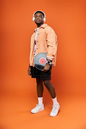 Foto de Elegante hombre con auriculares sosteniendo un registro sobre fondo naranja. - Imagen libre de derechos
