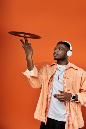 Foto de Hombre afroamericano guapo sosteniendo récord sobre fondo naranja vibrante. - Imagen libre de derechos