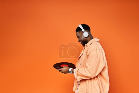 Téléchargez les photos : Un bel homme afro-américain dans un casque détient un record sur fond orange. - en image libre de droit