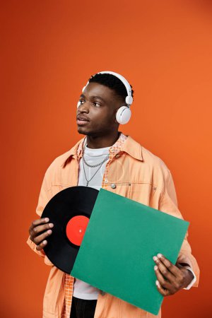 Stilvoller Afroamerikaner mit Kopfhörern, der eine Schallplatte in der Hand hält.