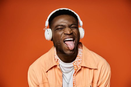 Jeune homme afro-américain élégant avec des écouteurs qui sortent sa langue.