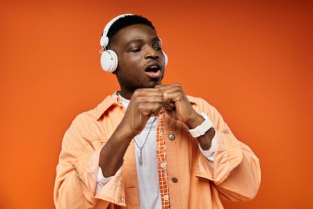 Ein modischer junger afroamerikanischer Mann trägt Kopfhörer vor orangefarbenem Hintergrund.