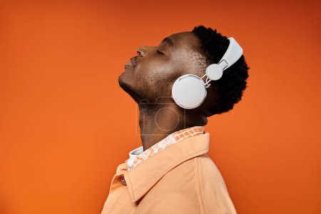 Photo for Stylish young man with headphones gazes at orange background. - Royalty Free Image