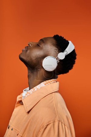 Stylish African American man in headphones on vibrant orange background.