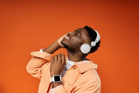 Ein modischer junger afroamerikanischer Mann trägt Kopfhörer auf orangefarbenem Hintergrund.
