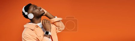 Téléchargez les photos : Un jeune homme afro-américain à la mode en tenue élégante lève la tête tout en écoutant de la musique. - en image libre de droit