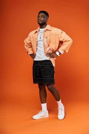Téléchargez les photos : Homme afro-américain élégant en chemise orange et short frappant une pose. - en image libre de droit