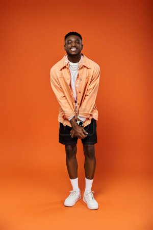 Photo for Stylish young man in orange shirt and shorts strikes a pose. - Royalty Free Image