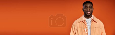 Téléchargez les photos : Jeune homme afro-américain en tenue élégante sort sa langue sur fond orange. - en image libre de droit