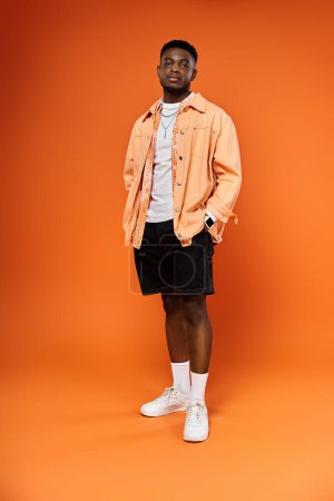 Photo for Fashionable African American man in orange jacket and shorts against orange backdrop. - Royalty Free Image