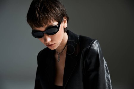 Stylish young woman in black leather jacket and sunglasses striking a pose.