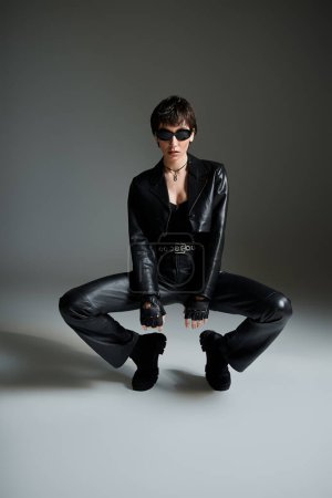 Foto de Young woman in black leather pants and sunglasses squatting. - Imagen libre de derechos