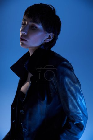Foto de Young woman striking a pose in a black leather jacket against a vibrant blue backdrop. - Imagen libre de derechos