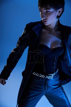 Confident woman in leather outfit poses against blue backdrop.