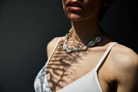 A woman adorned in a stylish seashell necklace poses gracefully.