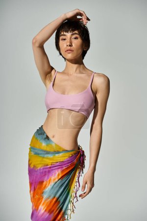Young woman showcases vibrant style in a pink bikini and colorful sarong.