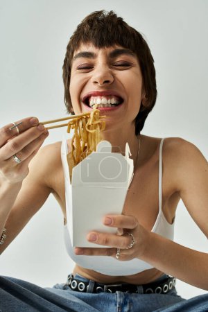 Téléchargez les photos : A stylish young woman gracefully enjoying noodles with chopsticks. - en image libre de droit