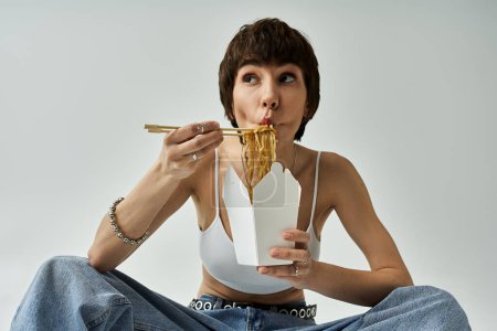 A stylish woman gracefully eats noodles with chopsticks.