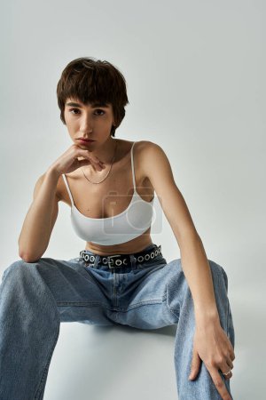 Stylish woman in white top and jeans sitting gracefully on floor.