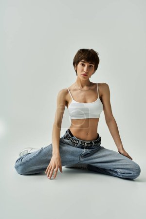 Young woman in white top and jeans sitting gracefully on floor.