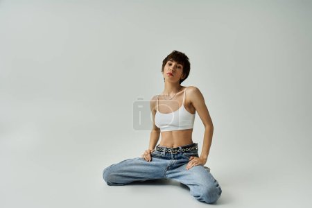 Téléchargez les photos : A young woman sits gracefully in jeans and a white tank top. - en image libre de droit