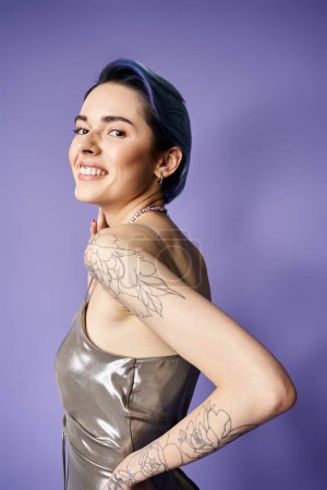 Young woman with short blue hair proudly displays a detailed tattoo on her arm in a silver party dress.