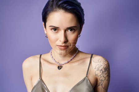 A stylish young woman with short blue hair showcases a tattoo on her arm while posing confidently in a silver party dress.