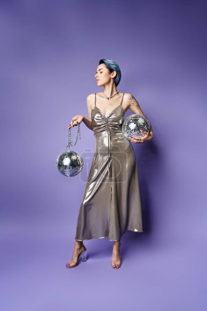 A young woman with short blue hair poses in a stunning silver dress while holding two sparkling silver balls.
