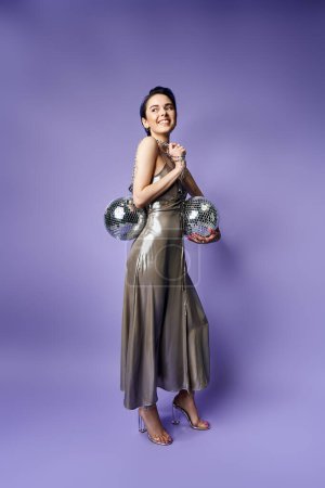 A young woman with blue hair poses gracefully in a silver party dress, holding disco balls