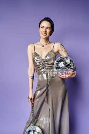 Young woman with short blue hair is striking a pose in a shimmering silver dress while holding a shiny disco ball.