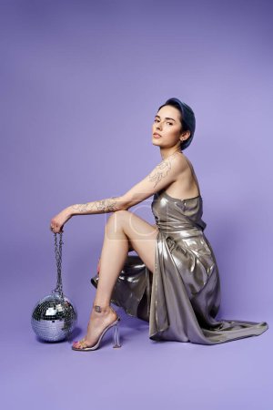 A young woman with short blue hair posing elegantly in a silver party dress
