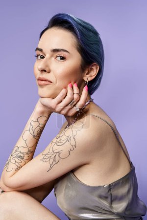 Téléchargez les photos : A young woman with short blue hair and arm tattoos strikes a pose in a silver party dress in a studio setting. - en image libre de droit