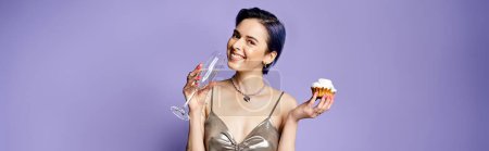 Téléchargez les photos : A young woman with short blue hair, dressed in a silver party dress, holding a cupcake and a glass of wine. - en image libre de droit