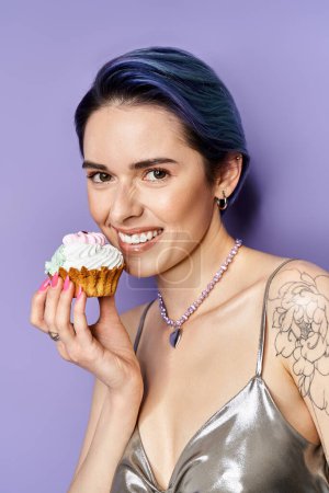 Foto de A pretty young woman with short blue hair posing in a silver party dress, holding a cupcake in front of her face. - Imagen libre de derechos