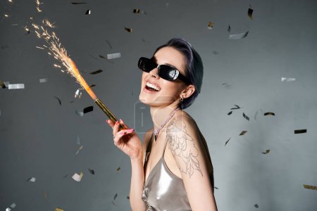 Stylish woman with short blue hair wearing sunglasses, holding sparkler.