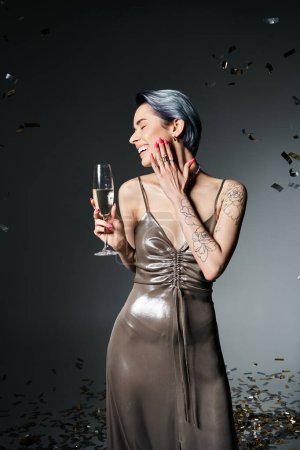 Stylish woman with blue hair enjoys a glass of champagne in a stunning silver dress at a party.