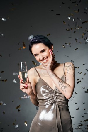 Young woman with short blue hair, radiantly adorned in a silver dress, elegantly holds a champagne glass in a stylish pose.