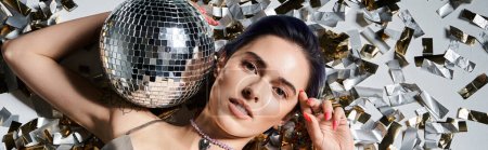 Téléchargez les photos : A pretty young woman with short blue hair holds a disco ball in front of her face, surrounded by a silver party dress. - en image libre de droit