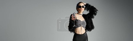 Foto de Young woman with short dyed hair looking stylish in a skirt and jacket, holding a champagne glass in a studio setting. - Imagen libre de derechos
