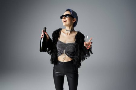 Foto de A stylish young woman with short dyed hair, wearing a black top and leggings, holds a champagne bottle - Imagen libre de derechos