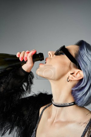 A stylish young woman with short blue hair drinks from a bottle in a vibrant studio setting.