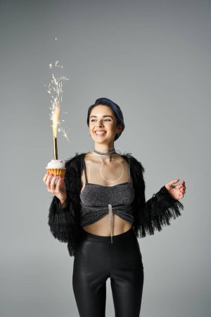 A young woman joyfully holding a cupcake with a sparkler, celebrating a birthday in a stylish setting.