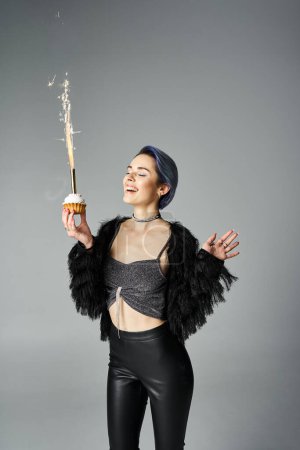 A young woman with short dyed hair wearing black pants and a crop top, playfully holds a sparkler in a studio setting.