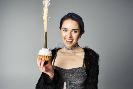 A stylish young woman with short dyed hair holding a cupcake topped with a delicate feather.