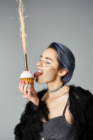 A young woman with vibrant blue hair holding a delicious cupcake in a fashion-forward pose.