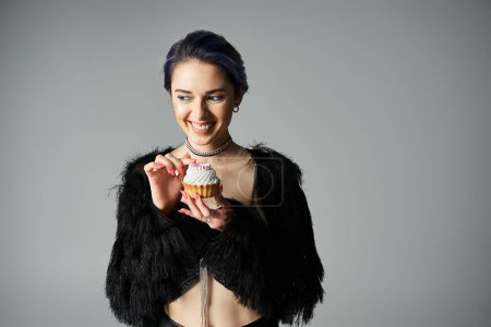 Photo for A pretty young woman with short dyed hair holds a colorful cupcake in her hands, admiring its intricate design. - Royalty Free Image